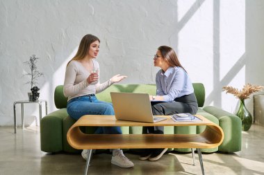 Terapi seansında genç ve gülümseyen kadın hasta psikolog sosyal terapist ile birlikte kanepede oturuyor. Sağlık hizmetleri gençlik yardımı, psikolojik hizmetler, psikoterapi kavramı