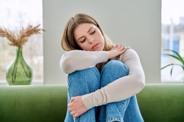 Evdeki kanepede oturan mutsuz, üzgün genç bir kadın, yüzü yakın çekim. Duygusal fiziksel acı çeken üzgün bir kadın. Sorunlar ruhun ve bedenin sağlığı, gençlik kavramı