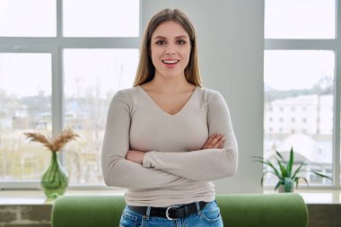 İç mekanda kollarını kavuşturarak poz veren kendinden emin genç bir kadının portresi. Gülümseyen mutlu 20 'li yaşlarda, sarışın, uzun saçlı, kameraya bakan bir kadın. Güzellik sağlık yaşam tarzı gençlik kavramı