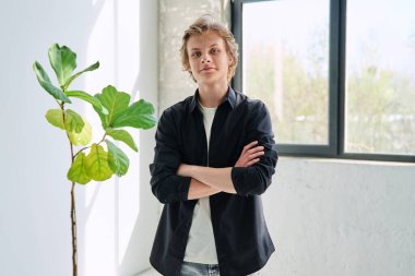 Oturma odasında kollarını kavuşturmuş, kendinden emin gülümseyen bir gencin portresi. Yakışıklı, mutlu, sarışın adam kameraya bakıyor. Ergen, erkek 16-17 yaşlarında, ergen, yaşam tarzı, boş zaman