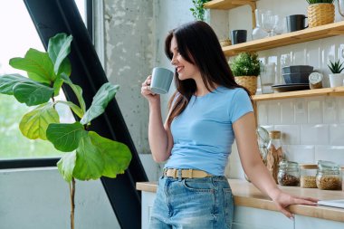 30 'lu yaşlardaki güzel, mutlu bir kadının portresi. Mutfakta bir fincan kahve, profil manzarası. Yaşam tarzı, ev hayatı, insan kavramı.