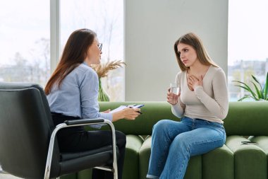 Bireysel terapi seansında kadın psikolog sosyal danışman ile konuşan genç bir kadın uzman ofisinde kanepede yan yana oturuyor. Psikoloji danışmanı zihinsel yardım desteği