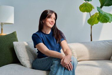 Oturma odasındaki kanepede oturan güzel esmer kadının portresi. Gülümseyen çekici 30 'lu yaşlardaki kadın gözlerini kaçırıyor. Güzellik, yaşam tarzı, kadın konsepti