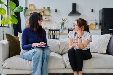 Kadın sosyal hizmet görevlisi, ruh sağlığı uzmanı orta yaşlı bir kadınla görüşüyor, oturma odasındaki kanepede yan yana oturuyor. Sosyal hizmetler, psikoloji, destek, yardım, insan kavramı