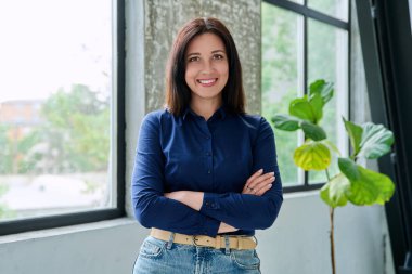 Güzel, gülümseyen, pozitif, kendine güvenen esmer kadının portresi. Pencere kenarında, çapraz kollu kameraya bakıyor. Güzellik, iş, iş, 30 'ların insanları kavramı