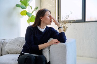 Ciddi derecede yorgun orta yaşlı bir kadın pencereden dışarı bakıyor, evinde kanepeye oturuyor, profil görüşü var, fotokopi çekiyor. Dinlen, rahatla, duygular, akıl sağlığı, olgun insanlar konsepti