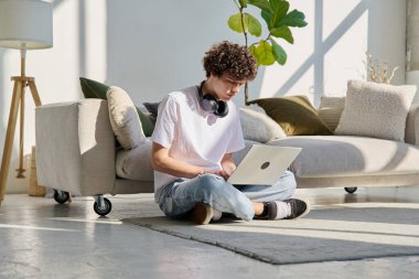 Evdeki kanepenin yanında dizüstü bilgisayarda yazan yakışıklı bir erkek portresi. Kıvırcık, güler yüzlü, 20 yaşında bir öğrenci. Yaşam tarzı, eğitim, teknoloji, gençlik kavramı