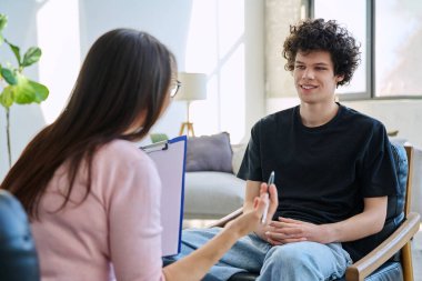 Zihinsel terapi seansında gülümseyen genç erkek hasta uzman psikolog psikoterapist danışman sosyal hizmet görevlisiyle konuşuyor. Hizmet psikolojisi psikoterapi desteği