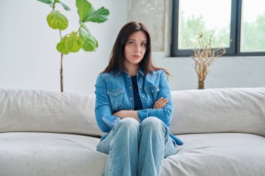 Oturma odasındaki kanepede oturan güzel esmer kadının portresi. Kollarını kavuşturup kameraya bakan 30 'lu yaşlarda çekici bir kadın. Güzellik, yaşam tarzı, kadın konsepti