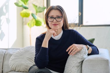 Orta yaşlı, güzel bir kadının portresi. Kanepede oturuyor. Gözlüklü, çekici, olgun bir kadın. Güzellik, sağlık, yaşam tarzı, insan kavramı