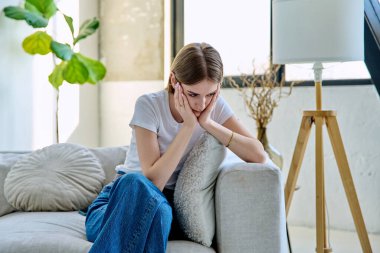Üzgün, hayal kırıklığına uğramış, 17-18 yaşlarında bir genç kız evinde kanepede oturuyor. Stres, depresyon, gençlik, gençlik krizi, gençlerin akıl sağlığı konsepti