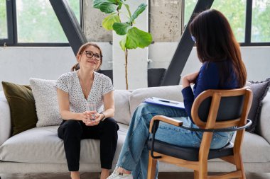 Zihinsel terapi seansı, orta yaşlı iş kadını hasta profesyonel psikolog psikoterapist zihinsel terapistle konuşuyor, kanepede yan yana oturuyor. Psikoloji psikoterapi danışmanlık konsepti