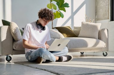 Evdeki kanepenin yanında dizüstü bilgisayarda yazan yakışıklı bir erkek portresi. Kıvırcık, güler yüzlü, 20 yaşında bir öğrenci. Yaşam tarzı, eğitim, teknoloji, gençlik kavramı