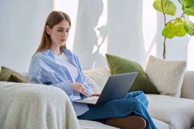 Evinde dizüstü bilgisayarı olan genç bir kadının portresi. Üniversite öğrencisi sınav için hazırlanıyor. Kadın dinleniyor. Sosyal medya blog alışverişi yapıyor.