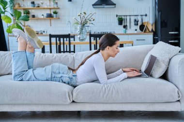 Evinde dizüstü bilgisayarla kanepede yatan genç bir kadının portresi. Üniversite öğrencisi sınava hazırlanıyor, bilgisayar başında yazı yazıyor, sosyal medya blogunu okuyor, internetten alışveriş yapıyor.