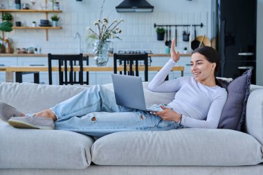 Genç kız video sohbet konferansı için dizüstü bilgisayar kullanıyor. Kanepede uzanmış web kamerasına bakıyor, bilgisayar ekranında konuşuyor. Eğitim eğitimi teknolojileri eğlence iletişimi gençlik kavramı