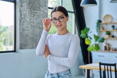 Gözlüklü, evde poz veren başarılı genç kızın portresi. Kameraya bakan uzun saçlı, gülümseyen genç bir bayan. Güzellik, sağlık, yaşam tarzı, gençlik kavramı