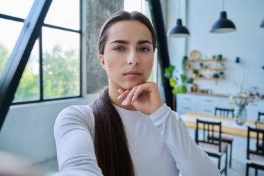 Web kamerasına bakan genç bir bayanın yakın plan selfie portresi. Evde 18-19 yaşlarında ciddi bir genç kız var. Güzellik, yaşam tarzı, gençlik kavramı