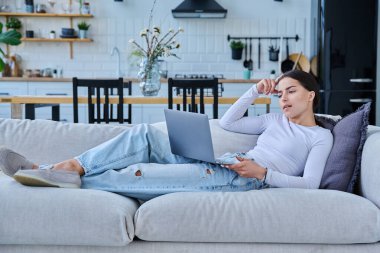 Genç kız video sohbet konferansı için dizüstü bilgisayar kullanıyor. Kanepede uzanmış web kamerasına bakıyor, bilgisayar ekranında konuşuyor. Eğitim eğitimi teknolojileri eğlence iletişimi gençlik kavramı