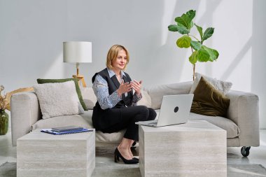 Orta yaşlı iş kadını evdeki kanepede oturan dizüstü bilgisayarla görüntülü konuşma görüşmesi yapıyor. Uzaktan görüşme, iş görüşmesi, online terapi oturumu, iş tele-teknoloji konsepti.