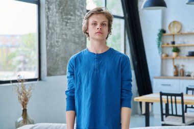 Evde kendine güvenen ciddi bir gencin portresi. Yakışıklı sarışın adam kameraya bakıyor. Gençlik yaşı, 16-17 yaş arası, ergen, yaşam tarzı, eğlence konsepti