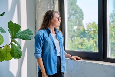 Orta yaşlı, sakin, pencereden dışarı bakan, gülümseyen olgun bir kadın hayal eden, profil manzaralı, kopyalayan bir kadın. Yaşam tarzı, orta yaşlı insanlar konsepti
