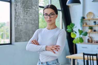Evde çapraz kollarla poz veren kendinden emin başarılı genç kızın portresi. Kameraya bakan uzun saçlı, ciddi ve güzel bir genç bayan. Güzellik, sağlık, yaşam tarzı, gençlik kavramı