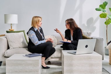 Zihinsel terapi seansı, orta yaşlı iş kadını hasta profesyonel psikolog psikoterapist zihinsel terapistle konuşuyor, kanepede yan yana oturuyor. Psikoloji psikoterapi danışmanlık konsepti