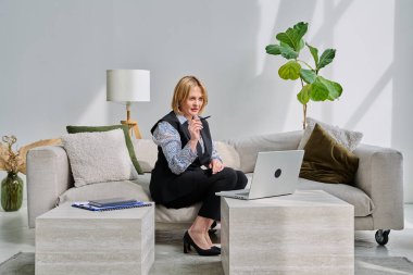 Orta yaşlı iş kadını evdeki kanepede oturan dizüstü bilgisayarla görüntülü konuşma görüşmesi yapıyor. Uzaktan görüşme, iş görüşmesi, online terapi oturumu, iş tele-teknoloji konsepti.