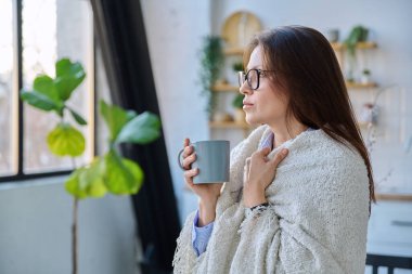 Rahat orta yaşlı kadın battaniyesinin altında ev içi pencerenin yanında, soğuk mevsim sonbahar baharı, ev konforu, yaşam tarzı, insan konsepti