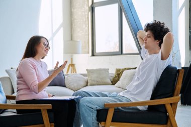 Genç erkek hasta, ofisinde oturan orta yaşlı kadın psikolog sosyal hizmet danışmanı ile konuşuyor. Gençlik psikoterapisi psikolojisi için ruh sağlığı psikolojik sosyal hizmetleri