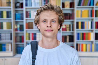 Kütüphanede kameraya bakan yakışıklı, kendine güvenen bir gencin portresi. 16-17 yaşlarında, sırt çantalı, kitap raflarıyla sınıfta poz veren genç bir erkek. Eğitim ergenlik bilgisi