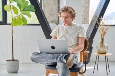 Evde oturup dizüstü bilgisayarla yazı yazan yakışıklı bir genç çocuk. Gençlik yaşı, ergenlik, yaşam tarzı, teknoloji konsepti