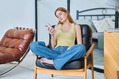 Genç, gülümseyen bir kadın sandalyesinde oturuyor. Akıllı telefon kullanıyor. Rahat, güzel bir kadın. Boş zaman sosyal iletişim eğitimi teknolojileri çalışma konsepti