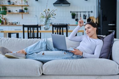 Genç kız video sohbet konferansı için dizüstü bilgisayar kullanıyor. Kanepede uzanmış web kamerasına bakıyor, bilgisayar ekranında konuşuyor. Eğitim eğitimi teknolojileri eğlence iletişimi gençlik kavramı