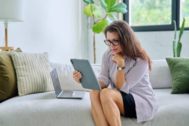 Uzaktan çalışan orta yaşlı bir kadın, video konferans görüşmeleri, evdeki ofiste dijital tablet kullanıyor. Psikoloji oturumu çevrimiçi öğretim koçluğu vlog işi iletişimi