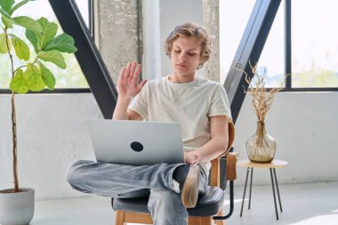16-17 yaşlarında genç bir çocuk bilgisayarını görüntülü sohbet konferansı için kullanıyor, online toplantı yapıyor, eğitici Webinar izliyor, evde oturuyor. Teknoloji, eğitim, e-öğrenme, lise