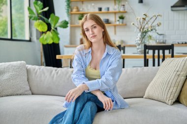 Evdeki kanepede oturan güzel, sakin, ciddi, genç bir kadının portresi. Genç, rahat kadın. 18-19-20 yaşlarında, sarışın. Oturma odasında uzun saçlı. Gençlik, yaşam tarzı, ev kavramı