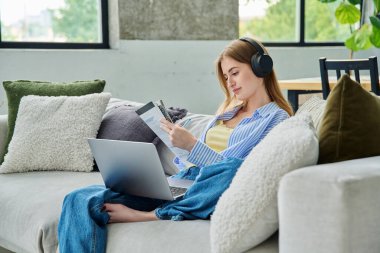 Kulaklıklı, dizüstü bilgisayarlı genç kız ders kitabı ile evdeki kanepede oturmuş online video dersi seyrediyor. Eğitim eğitimi teknolojileri gençlik iletişiminde eğlence amaçlı çalışır
