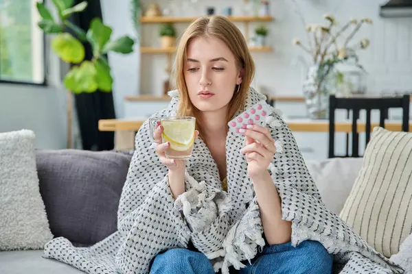 Ateşli, yaz mevsiminde battaniyenin altında hasta olan genç bir kadın evinde, koltukta oturmuş, bir paket sıcak çay ve limonla birlikte. Mevsimsel viral hastalıklar, hastalık, ilaçlar, tedavi, sağlık gençliği