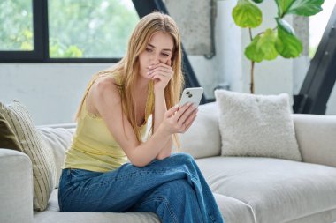 Üzgün, üzgün, genç bir kadın akıllı telefona bakıyor. Evdeki koltukta oturuyor, fotokopi çekiyor. İletişim kurmak için telefon kullanan bir kadın, eğitim için mobil uygulamalar sosyal ağlar