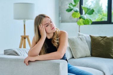 Evdeki kanepede oturan mutsuz, yorgun genç kadın. Duygusal fiziksel acı çeken üzgün bir kadın. Sorunlar ruhun ve bedenin sağlığı ve gençliğin sorunları