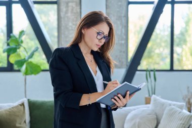 Siyah gözlüklü, orta yaşlı bir iş kadınının portresi. Ofisinde iş not defteri olan 40 'lı yaşlarda kendinden emin bir profesyonel kadın. İş yönetimi kariyeri olgun insanlar