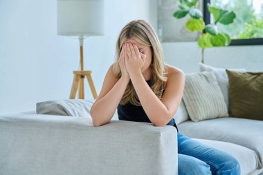 Evdeki kanepede oturan mutsuz, yorgun genç kadın. Duygusal fiziksel acı çeken üzgün bir kadın. Sorunlar ruhun ve bedenin sağlığı ve gençliğin sorunları