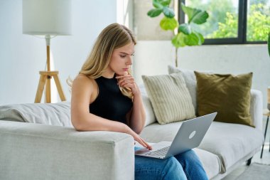 Genç ciddi bir kadının portresi kanepede oturuyor ve iç dizüstü bilgisayar kullanıyor. Üniversite öğrencisi sınav için hazırlanıyor bilgisayarlı kadın rahatlama sosyal medya blog alışverişini online olarak okuyun