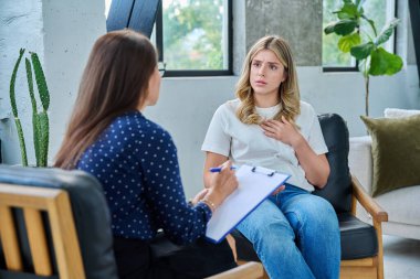 Üzgün genç kadın hasta terapi seansında kadın psikolog psikoterapist, ruh sağlığı danışmanı ve sosyal psikolog ile birlikte ofiste otururken gergin.