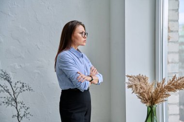 Ciddi bir şekilde kendinden emin orta yaşlı kadın camdan dışarı bakıyor, kolları çapraz, kopyalama alanı var. İş dünyası, dinlenme molası, duygular, akıl sağlığı, olgun insanlar konsepti
