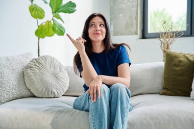 Oturma odasındaki kanepede oturan güzel, mutlu esmer kadının portresi. 30 'lu yaşlarda çekici bir kadın kameraya bakıyor. Güzellik, yaşam tarzı, kadın konsepti