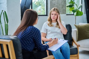 Üzgün genç kadın hasta terapi seansında kadın psikolog psikoterapist, ruh sağlığı danışmanı ve sosyal psikolog ile birlikte ofiste otururken gergin.