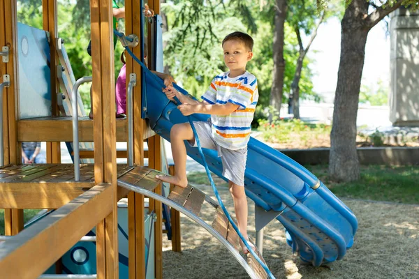 Ein Fröhlicher Junge Klettert Einem Seil Auf Den Spielplatz Mit — Stockfoto